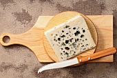 A wedge of blue cheese on a wooden board with a knife