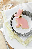 Rabbit-shaped biscuit with pink icing and small bell in tartlet tin