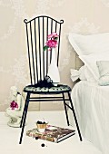 Pinkfarbene Rosen der Sorte Yves Piaget auf Frauenskulptur & in Vase auf romantischem Metallstuhl neben Bett