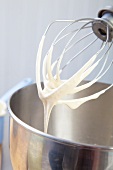 An egg whisk on a food processor with remnants of beaten egg white
