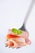 Sliced ham with an oregano leaf on a fork (close-up)