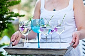 Frau hält Tablett mit mehreren Gläsern Lavendelwasser