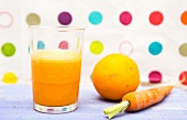 A glass of carrot and orange juice next to a fresh orange and a fresh carrot