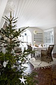 Mit weissen Sternen und Glaskugeln dekorierter Weihnachtsbaum; Esszimmer mit holzverkleideter, weisslackierter Tonnendecke und Mosaikparkett