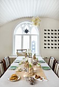Table festively set in delicate colours; dining room with luster of glass bubbles hanging from vaulted, wooden ceiling and arched window