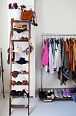 Old wooden ladder used as storage for ladies accessories; next to it a metal clothes rack with clothes hanging from it