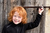 Red haired child in front of a wooden door