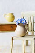 A few forget-me-not flowers in tiny jug on dolls' house chair in front of small wooden table