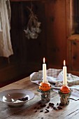 Selbstgemachte Kerzenständer mit brennenden Kerzen auf gespickten Orangen und Teller auf Holztisch in adventlicher Hüttenstimmung