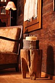 Candle lantern with knitted cover on tree trunk stool in front of comfortable armchair in wooden chalet