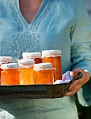 A woman holding a tray full of jars of jam