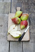 Several pears, whole and halved, on a chopping board with a knife