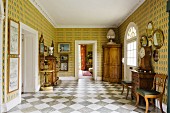 Spacious foyer with antique, 18th century furniture, boldly patterned wallpaper and diagonal, chequered marble floor tiles