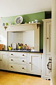 Küchenzeile einer Landhausküche mit weissen Unterschränken und eingebautem Gaskochfeld unter Abzug an grüner Wand