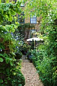 Lush vegetation in garden with gravel path leading to house with brick facade