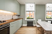 Grey kitchen counter and tone-on-tone wall in spacious modern kitchen; long, shabby-chic dining table in middle