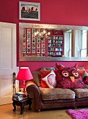 Large wall-mounted mirror with silver frame on hot pink wall above leather couch with large cushion shaped like owl