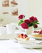 Gedeckter Tisch mit Erdbeerkuchen, Rosenstrauss und Kaffeegeschirr