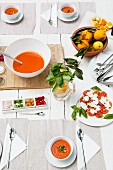 Gedeckter Tisch mit Gazpacho, Tomaten und Mozzarella, Orangen und Zitronen