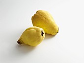 Two pear-shaped quinces on a white surface