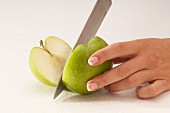 A woman cutting a green apple in half with a knife