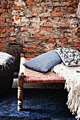 Scatter cushions on antique stool with woven seat in front of rustic brick wall