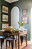 Blumen auf rustikalen Holztisch und Metallstühle mit Retro Flair in traditioneller Esszimmerecke mit gerahmten Bildern an grünen Wänden