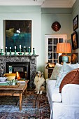 Sofa with white upholstery and rustic coffee table on rug in front of open fireplace in traditional living room