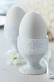 Eggcups trimmed with white lace ribbon as romantic decorations on breakfast table