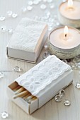 Matchboxes covered in white paper and decorated with lace trim and decorated tealights