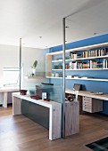Half-height glass wall with steel supports between living area and office space with shelving on blue-painted wall