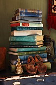 Old child's shoes and brass ornament in front of stacked books on blue trunk
