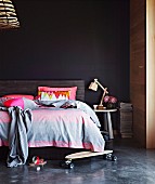 Skateboard on floor in front of double bed with headboard against black wall