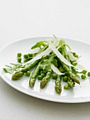 Asparagas and peas with parmesan shavings on a white plate
