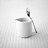 White jug of milk with a teaspoon on a white textured background
