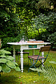 Folding garden chair and white-painted, shabby-chic table with turned legs in garden