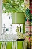 Glass carafes and green retro lamp with rabbit figurine as base on windowsill