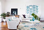 White wicker armchairs and sofa around white table in living room with turquoise patterns on Florence Broadhurst wallpaper and rug