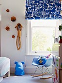 Blue accents in child's bedroom with patterned Roman blind, dog figure and classic rocking chair; striped sock monkey on wall