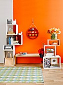 Stacked, cubic shelving modules & round ornamental shelving on wall above cloakroom bench against orange wall