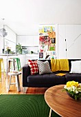 Open-plan interior with simple, white kitchen and living area decorated with colourful children's' books, patterned scatter cushions and vintage stools