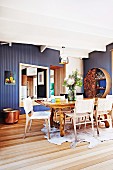 Dining area with animal-skin rug, rustic table and woven chairs in front of blue-painted wooden wall