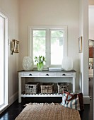 Large lanterns and flowers on console table with drawers and storage baskets below window