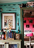 Bücher und maritime Deko an türkisfarbener Wand über Vintage-Kommode; seitlich Blick nach draußen auf pinkfarbene Wand