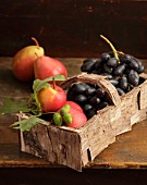 Spankorb mit Birkenrinde umwickelt, gefüllt mit Birnen und Weintrauben