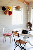 Various chairs in front of round table below arc lamp; colourful hats on Bauhaus coat rack on wall