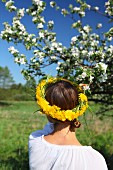 Woman wearing head wreath of dandelions in front of blossoming apple tree