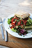 Mediterranean salad combination, overflowing from a ciabatta sandwich, on a plate