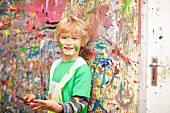 Boy with paintbrush against wall spattered with paint