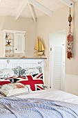 Union Flag scatter cushions on double bed and ensuite bathroom behind half-height wall with maritime decor